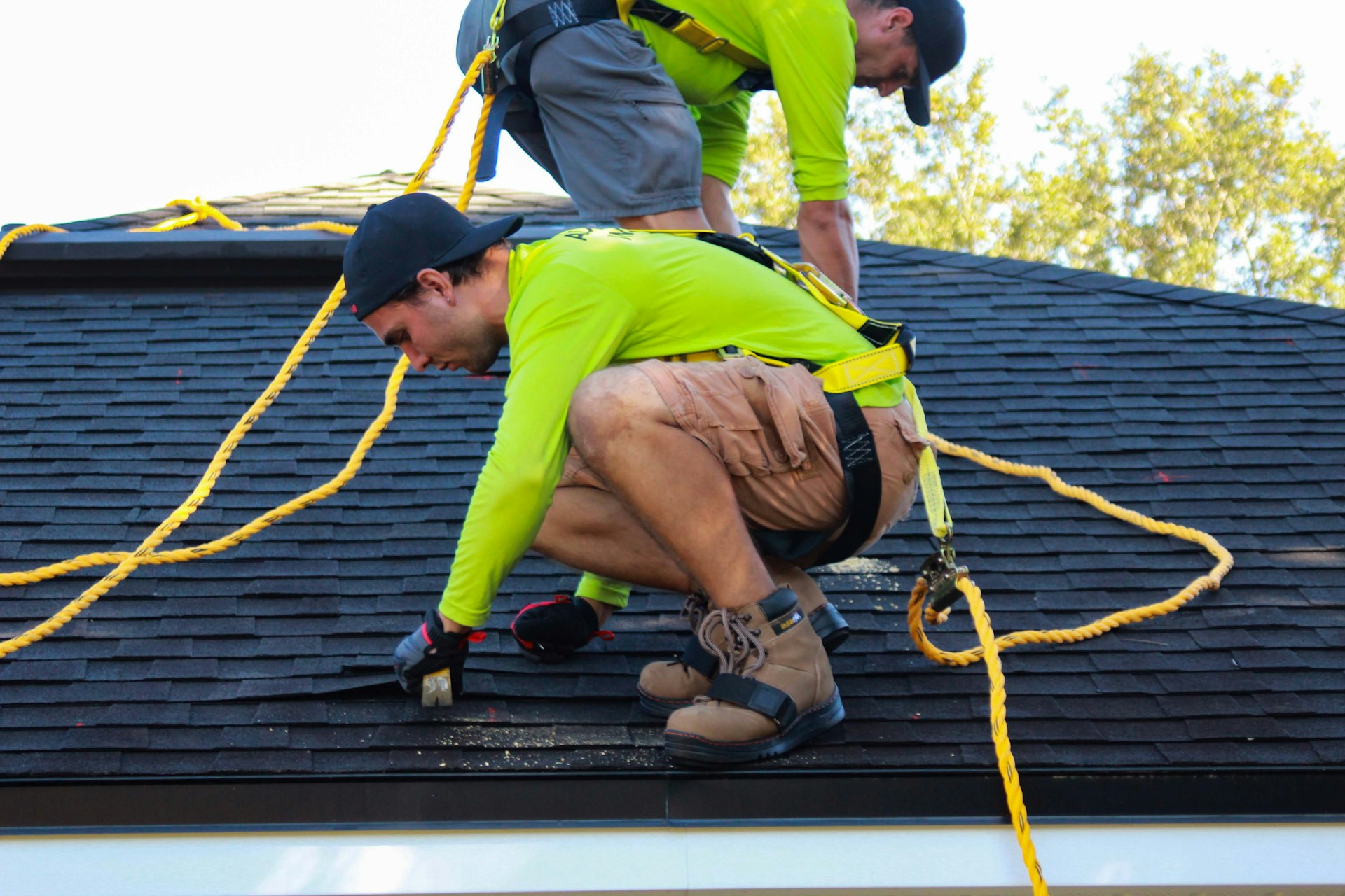 Professional roofers performing roof repair with safety harnesses